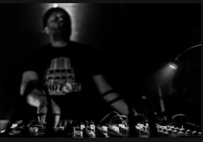 Black-and-white photograph of a DJ performing at a mixing desk