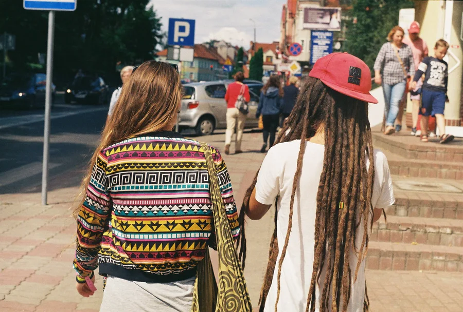 Two people in colourful clothing walk away along a city street.