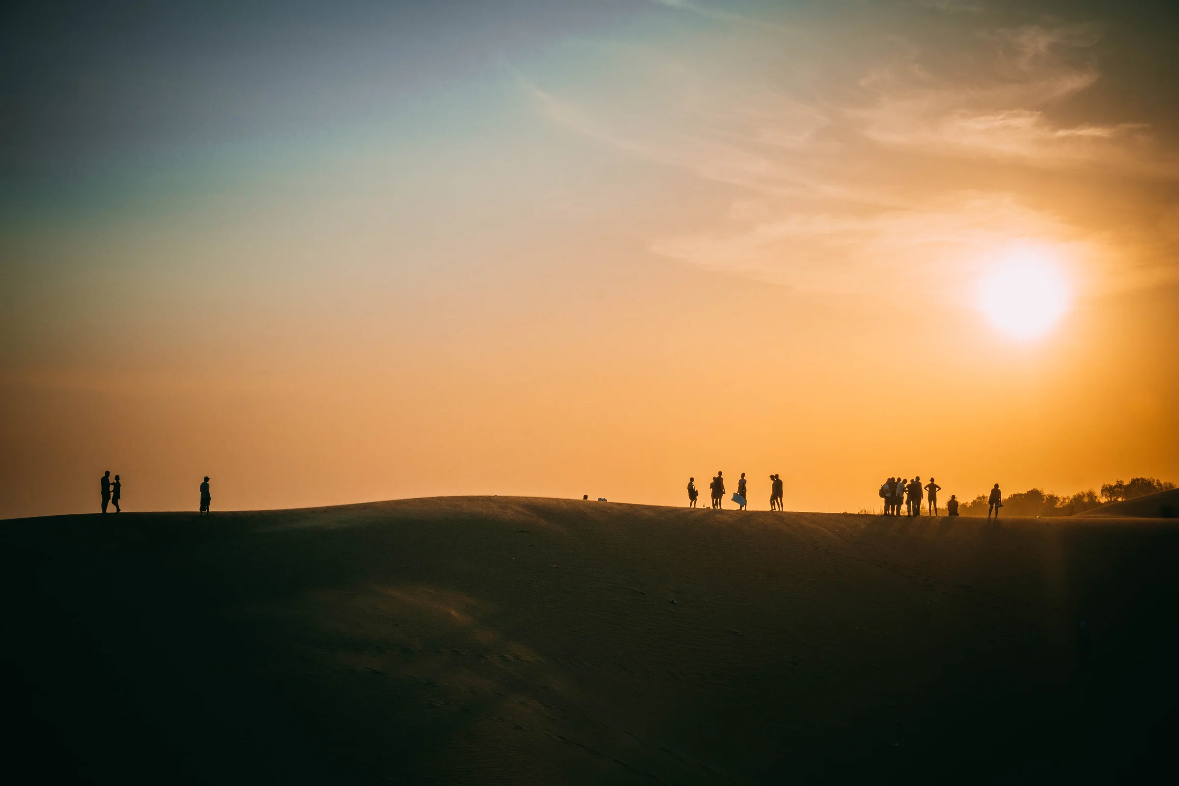 Silhouettes on the crest of dunes beneath the last light of a glowing sunset