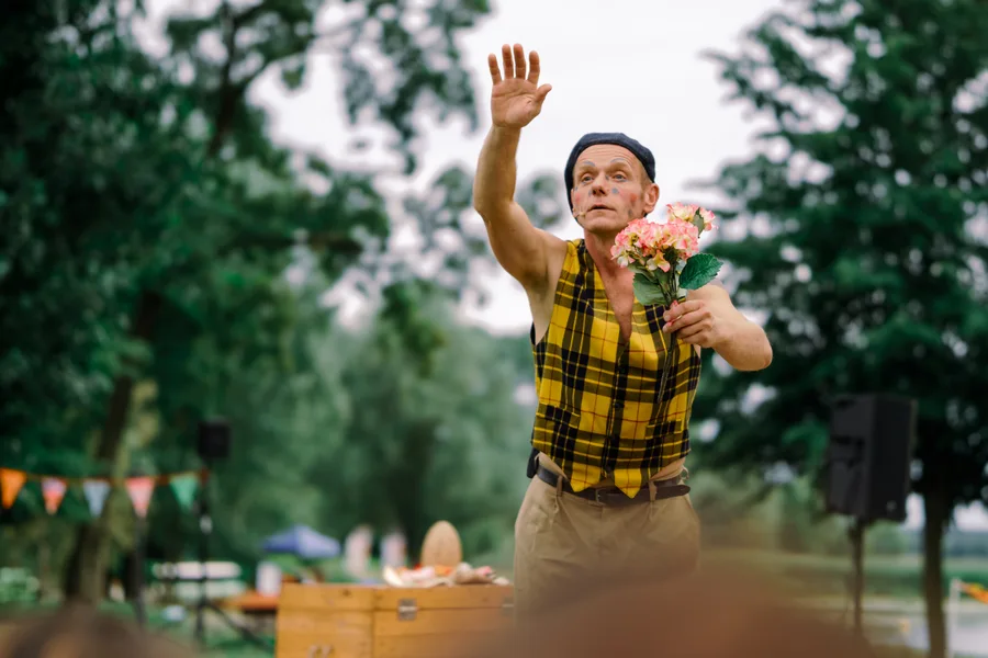 A performer in yellow checks raises a hand while holding flowers.