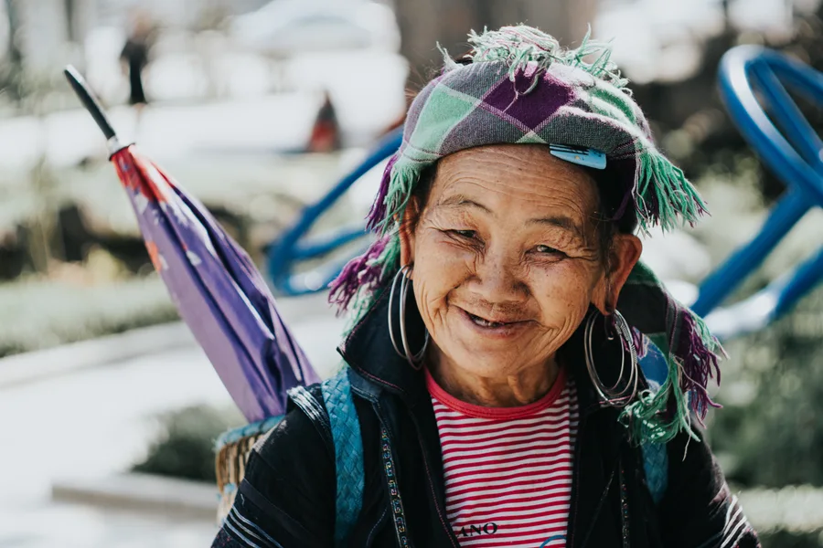 A smiling woman wearing a colourful headscarf beneath an umbrella.
