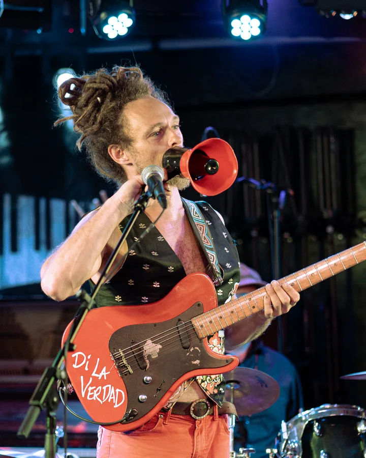 A musician holds a red megaphone while playing a red guitar on stage.