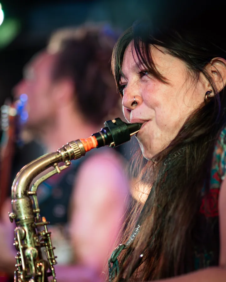 Close portrait of a saxophonist performing under coloured stage lights.