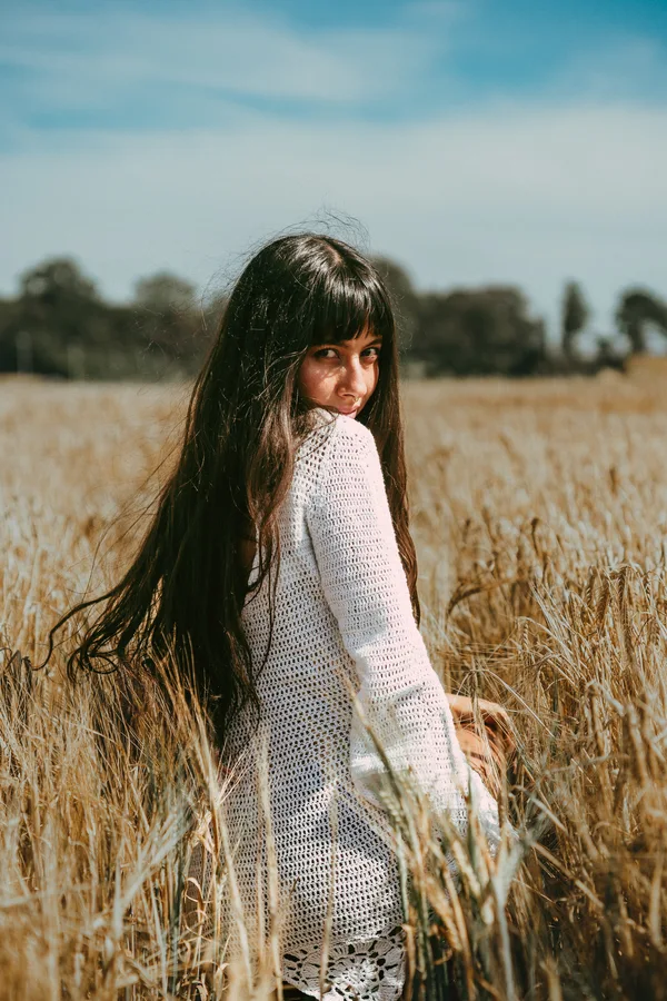 A woman in a white crochet dress looks back across a golden field.